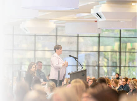 A person speaking a microphone and podium in front of a room full of people.